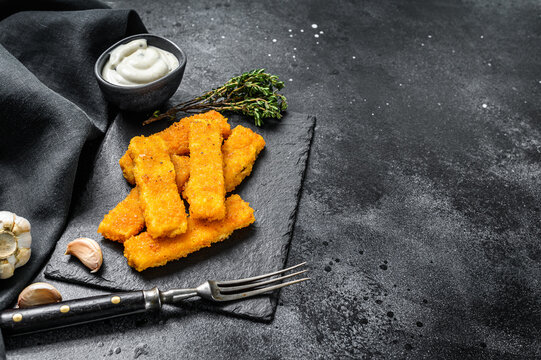 Oven baked crumbed fish sticks made from white fish.  Black background. Top view. Copy space