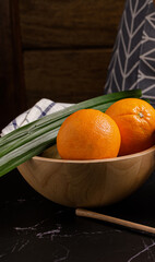Whole fresh orange in wooden bowl on black stone table.