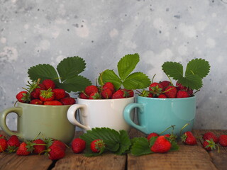 Summer berry theme.Strawberry in three porcelain cups on a wooden table. Copy space.