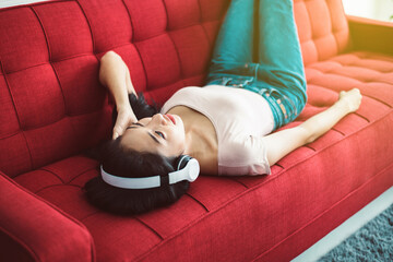 Beautiful young asian woman listening to music with headphones while lying on sofa