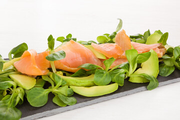 Salmon, avocado and green salad on black tray.