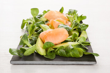 Salmon, avocado and green salad on black tray.