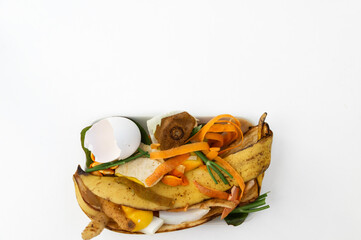 Organic waste in a plate on a white background. Vegetable scraps, peel of banana, carrots, kiwi, lemon, pumpkin seeds, eggshell. flatlay, copy space. Selective focus.