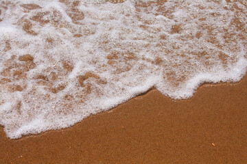Fototapeta na wymiar Foamy water comes to the sandy beach. The texture of the sandy beach