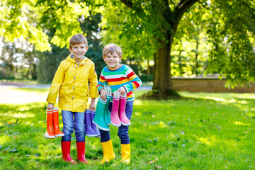 Two little kids boys, cute siblings with lots of colorful rain boots. Children in different rubber boots and jackets. Footwear for rainy fall. Healthy twins and best friends having fun outdoors