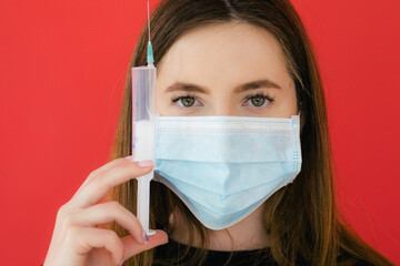 COVID-19 Pandemic Coronavirus Young girl on red background face mask protective holding a syringe. Coronavirus Disease 2019.