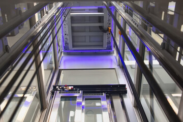 An elevator rises in a glass shaft. Photo of the elevator below.