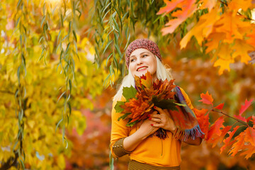 Portrait of cheerful young woman with autumn leafs in front of foliage making selfie