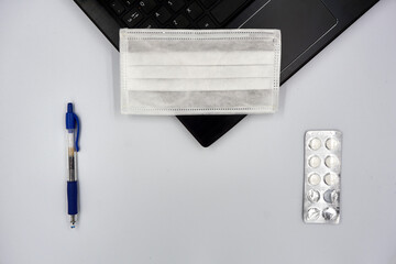 Pen, surgical face mask, medicine pills and laptop over white background