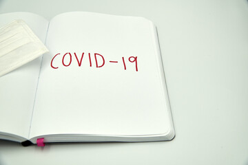 Covid 19 writing on a blank notebook with surgical mask over white background