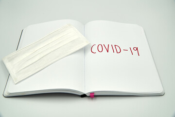 Covid 19 writing on a blank notebook with surgical mask over white background