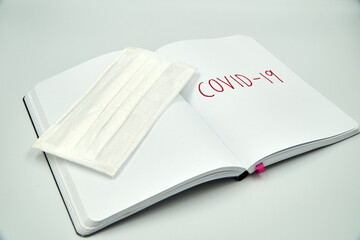 Covid 19 writing on a blank notebook with surgical mask over white background