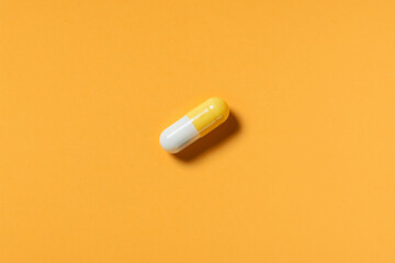 yellow and white pill or capsule lies on orange background top view copy space