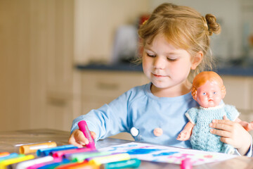 Fototapeta premium little alone toddler girl painting with felt pens during pandemic coronavirus quarantine disease. Happy creative child with old vintage doll, homeschooling and home daycare with parents