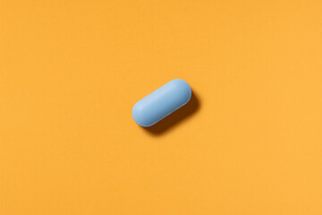 Blue pill or capsule lies on orange background top view copy space