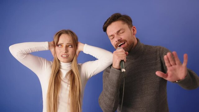 Young woman can't take the noise of her boyfriend singing. Closing the ears with hands and making annoyed face expression
