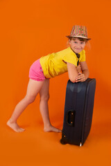 a beautiful happy girl in a Panama hat or hat travels with a blue suitcase on an orange background