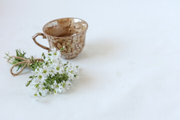A Cup of coffee with a bouquet of delicate wild flowers on a white background, side view, place for the inscription.