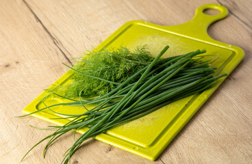 Green dill and onions on a wooden table.