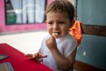 cute little toddler kid in bib sitting at a table on a street terrace cafe and eating  food
