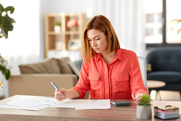remote job, technology and people concept - young woman with calculator and papers working at home...