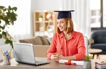 e-learning, education and people concept - happy smiling female graduate student in mortarboard...