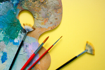 Painting palette detail and paint brushes on a yellow background