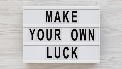 'Make your own luck' on a lightbox on a white wooden background, top view. Flat lay, from above, overhead.
