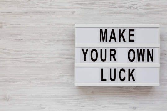 'Make your own luck' on a lightbox on a white wooden surface, top view. Flat lay, from above, overhead. Space for text.