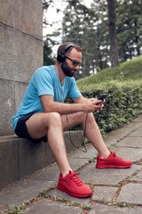 Fototapeta premium Modern sporty adult man making pause in the park after exercising / running and jogging.