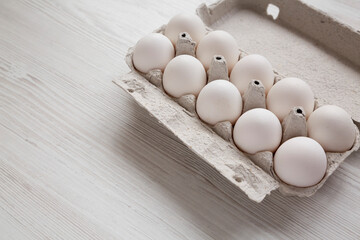 Uncooked Organic White Eggs in a paper box on a white wooden background, side view. Space for text.