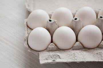 Uncooked Organic White Eggs in a paper box on a white wooden background, side view. Copy space.
