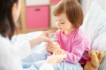 healthcare, children and people concept - doctor giving medicine to little sick african american girl in bed at home