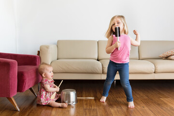 Little girl singing into hairbrush while baby sister plays music with kitchen utensils