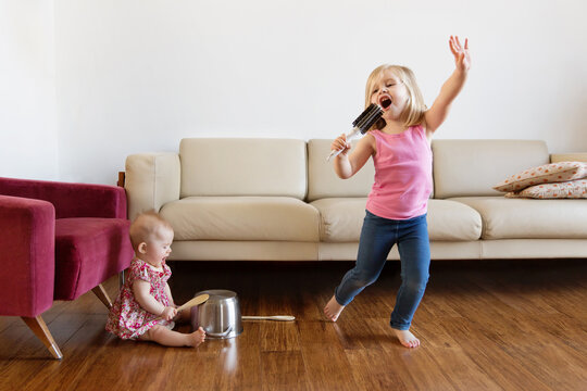 Girl singing with hairbrush while baby sister playing music with utensils