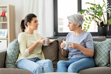 family, generation and people concept - senior mother with adult daughter drinking coffee or tea...