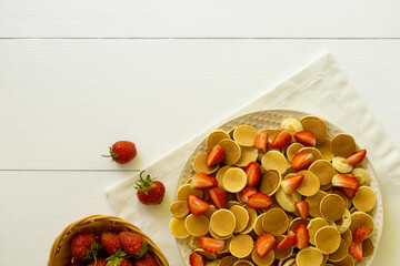 Tiny pancakes with strawberry on a white wooden background. Space for text