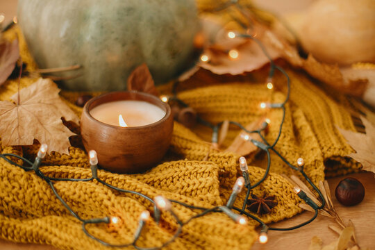 Pumpkins, autumn leaves, candle, warm lights and nuts on yellow knitted sweater on rustic background.Hello autumn. Cozy moody image. Happy Thanksgiving