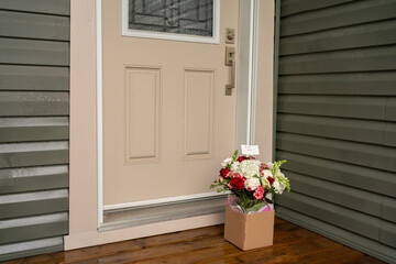A bouquet of red white flowers in a carton box on a porch doorstep of a house. Surprise contactless delivery of flowers.