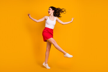 Fototapeta na wymiar Full size profile photo of funny cheerful lady raise hands leg rejoicing summer weekend warm breeze blowing wear white tank-top red skirt shoes isolated yellow bright color background