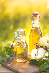 Two glass bottles of apple cider vinegar and fresh ripe apples on a wooden nature background. Copy space