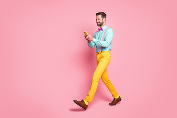 Full length body size profile side view of his he nice attractive classy chic cheerful focused brunet guy boyfriend using digital gadget app 5g chatting isolated over pink pastel color background