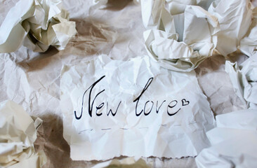 Hand written words "new love" on piece of paper on crumpled paper background