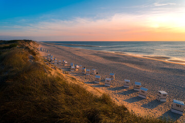 Sand dunes with beach and beach chairs at Sylt Ellenbogen during sunset with beatiful yellow sky