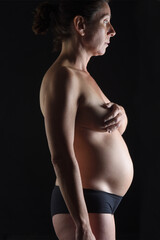 portrait of pregnant woman naked on black background, six months;