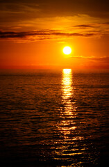 Una puesta de sol naranja con el sol reflejado en el mar.