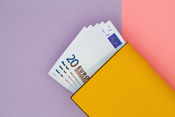 Close-up of yellow wallet with 20 Euro banknotes on a colored background