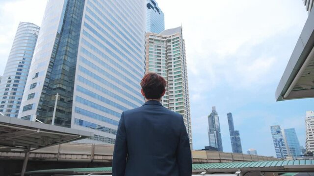 Back view of the Thoughtful Businessman wearing a Suit looking out while standing near modern Office Building background. 4K Slow Motion Corporate.