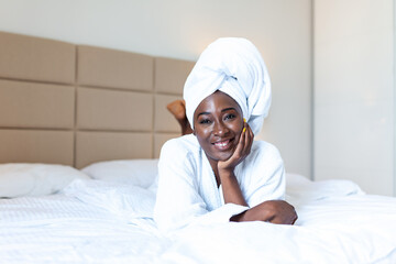 Positive start to the day . Smiling african young woman lying on bed in bathrobe. African american woman relaxing on the bed after bath and looking at the camera