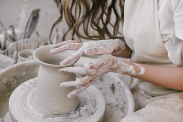 Young beautiful woman with long curly hair in white apron creating handmade ceramic bowl in a pottery.
